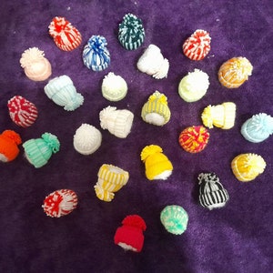 Könnte beinhalten: Eine Sammlung von 25 bunten Strickmützen mit Bommeln. Die Mützen sind in einem Kreis auf einer violetten Oberfläche angeordnet.