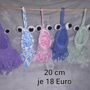 Könnte beinhalten: Fünf gehäkelte Hängetaschen mit Fransen, jede mit zwei schwarzen Augen. Die Taschen sind lila, blau-weiß, rosa, blau und grün. Der Text unter den Taschen lautet "20 cm je 18 Euro".