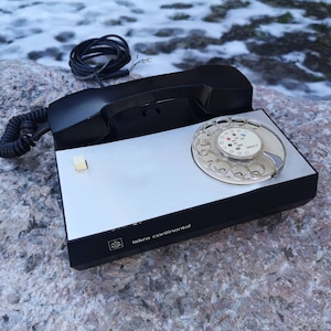 May include: A black rotary phone with a silver faceplate and a black cord. The phone has a white button and the text "Iskra Continental" on the faceplate.