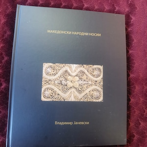 May include: A dark blue book cover with the title "македонски народни носии" and the author "Владимир Јаневски". The cover features a gold embroidered design.