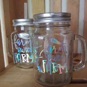 May include: Two clear glass mason jars with silver lids and handles. Both jars have a holographic sticker that says "farm sweet farm".