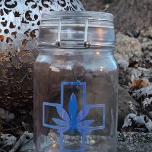 Peut inclure: Un pot en verre transparent avec un motif de feuille de cannabis bleu et blanc. Le pot a une fermeture à fermoir métallique.
