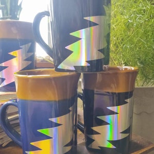 May include: Four ceramic mugs with a brown top and blue bottom. Each mug has a holographic lightning bolt design.