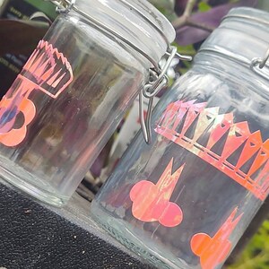Peut inclure: Deux bocaux en verre transparent avec des motifs de couronne et de nuage roses et blancs. Les bocaux ont des couvercles en métal avec un mécanisme de verrouillage.
