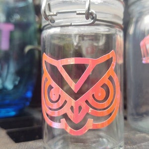 Peut inclure: Un pot en verre transparent avec un couvercle en métal et un autocollant d'un hibou rose sur le devant. Le pot a un joint en caoutchouc autour du couvercle.