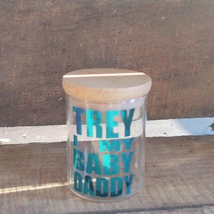 Peut inclure: Un bocal en verre transparent avec un couvercle en bois. Le bocal a un autocollant en vinyle bleu qui dit "Trey is my baby daddy".