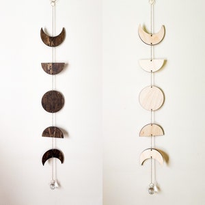 May include: Two wooden moon phase wall hangings with a crystal at the bottom. The left side features dark wood and the right side features light wood.