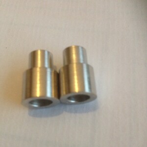 May include: Two silver metal spacers, each with a cylindrical shape and a smooth, polished finish.
