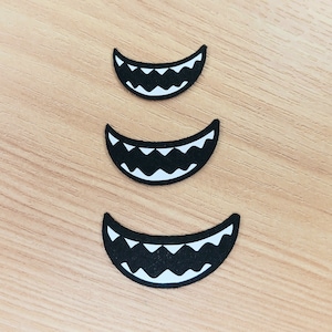 May include: Three black and white felt mouth shapes with jagged teeth, arranged in a vertical stack from largest to smallest.