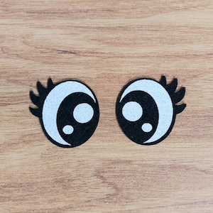 May include: Two black felt googly eyes with white glitter and black pupils on a wood background.