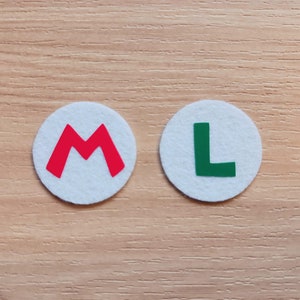 May include: Two white felt circles with red and green letters. The left circle has a red "M" and the right circle has a green "L".