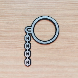 May include: A black and silver monocle patch with a chain detail. The patch features a circular frame with a silver glitter outline and a chain of five links. The design is set against a light wood grain background.