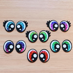 May include: Assortment of colorful googly eyes with black pupils and white irises. The eyes are made of plastic and have a shiny, iridescent finish.