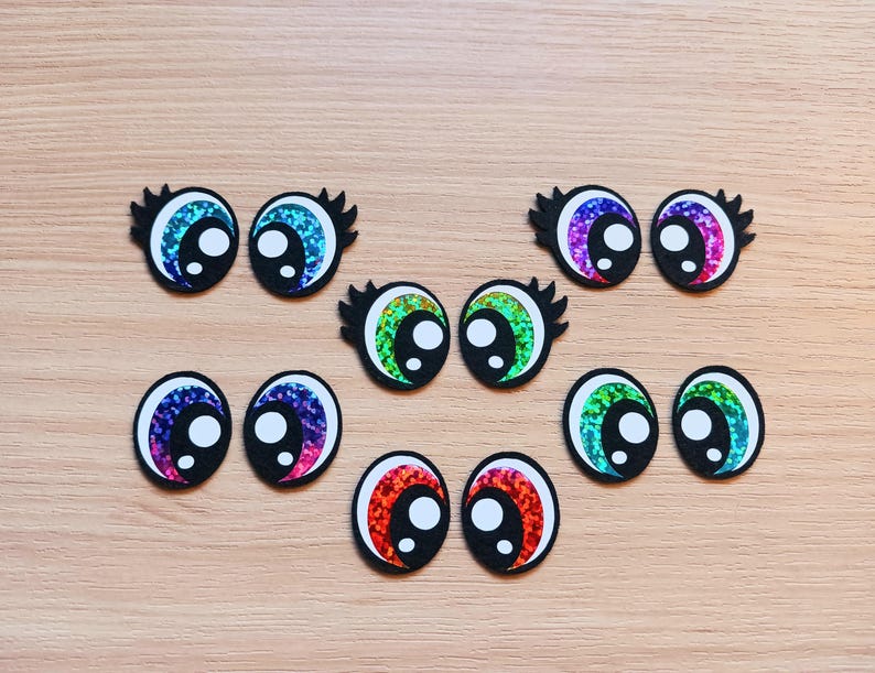 May include: Assortment of colorful googly eyes with black pupils and white irises. The eyes are made of plastic and have a shiny, iridescent finish.