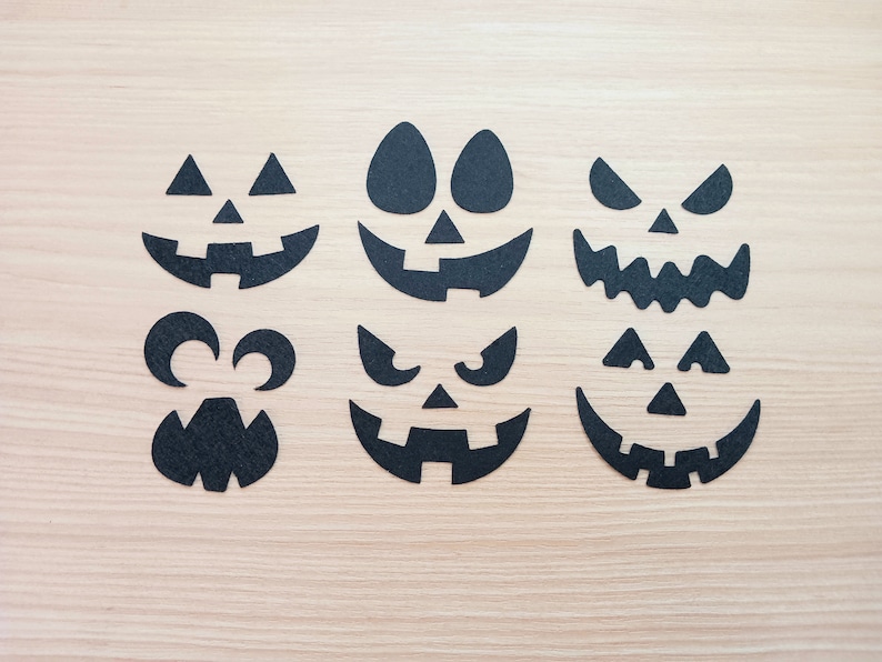 May include: Six black paper cutouts of different jack-o'-lantern faces on a light wood background.