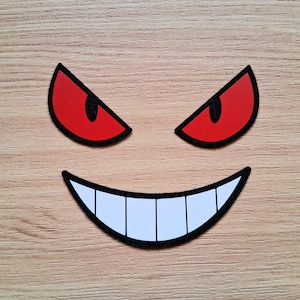 May include: A red and black cartoon face with a wide, toothy grin. The eyes are red with black pupils.