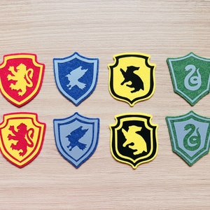 May include: Eight felt patches in the shape of shields, each representing a different Hogwarts house. The shields are yellow, red, blue, green, and black with different animal and creature symbols.