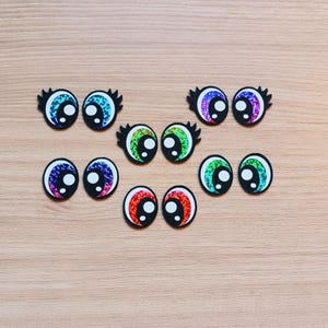 May include: Assortment of colorful googly eyes with black pupils and eyelashes. The eyes are made of plastic and have a shiny, iridescent finish.