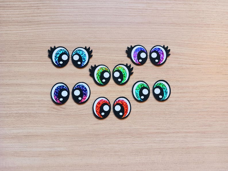 May include: Assortment of colorful googly eyes with black pupils and eyelashes. The eyes are made of plastic and have a shiny, iridescent finish.