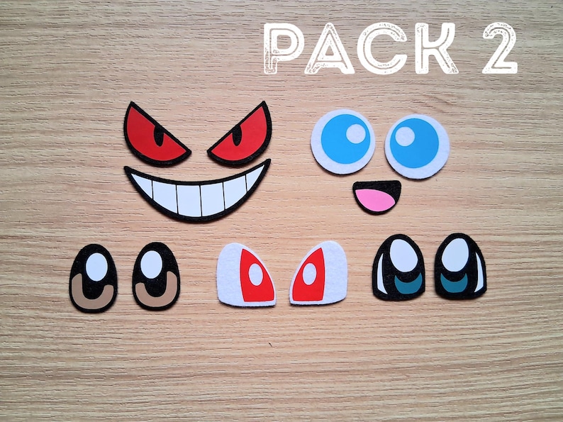 May include: A collection of cartoon face cutouts, including eyes, mouths, and eyebrows. The set features various expressions with colors like red, white, black, blue, and pink. The text "PACK 2" is visible at the top.