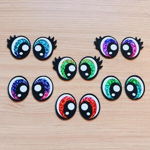 May include: Assortment of colorful googly eyes with black pupils. The eyes are made of glitter and have a shiny finish.