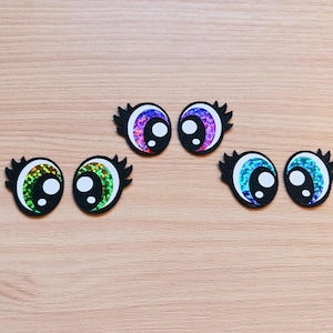 May include: Six colorful googly eyes with black outlines and white pupils. The eyes are made of glitter paper and have a variety of colors, including green, blue, and purple.