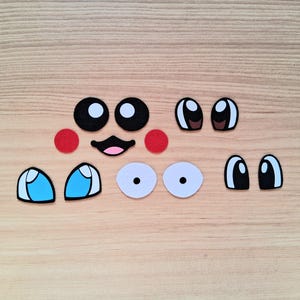 May include: A collection of felt face pieces, including black and white eyes, red cheeks, and a smiling mouth. Various eye shapes and colors are present, ideal for crafting or DIY projects.