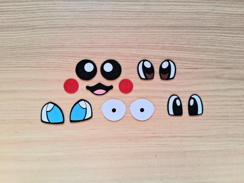 May include: A collection of felt face pieces, including black and white eyes, red cheeks, and a smiling mouth. Various eye shapes and colors are present, ideal for crafting or DIY projects.