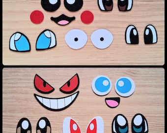May include: A selection of colourful felt facial features, including eyes, mouths, and cheeks, arranged on a wooden surface. The pieces are in various shapes and sizes, with a cartoonish aesthetic. The colour palette includes black, white, red, and blue.