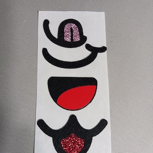 May include: A set of three black felt face stickers with glitter accents. The stickers include a mouth, a nose, and a pair of eyes. The mouth is red, the nose is pink, and the eyes are black.