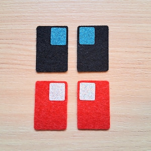 May include: Four felt squares with different colored squares in the center. Two squares are black with a light blue square in the center. Two squares are red with a white square in the center.