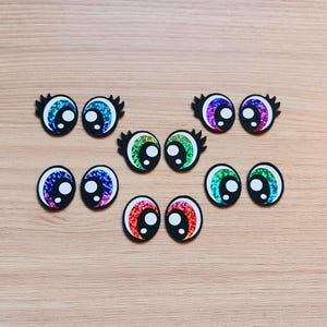 May include: Assortment of colorful googly eyes with black outlines. The eyes are made of iridescent material and have a variety of colors, including blue, green, purple, and red.