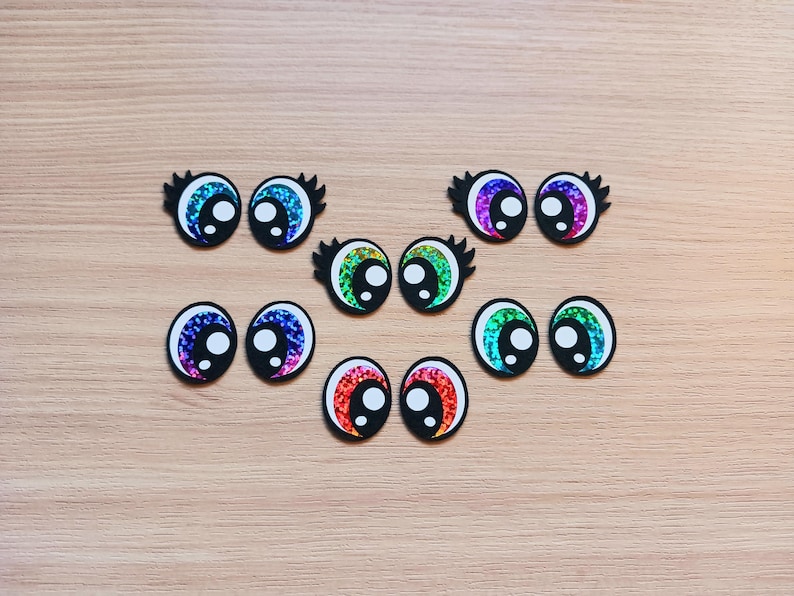 May include: Assortment of colorful googly eyes with black outlines. The eyes are made of iridescent material and have a variety of colors, including blue, green, purple, and red.