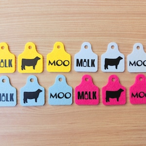 May include: Nine felt tags in three colors: yellow, blue, and pink. Each tag has a different design: a milk bottle, a cow, or the word "MOO".