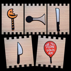 May include: Five Halloween-themed cutouts on wooden blocks. Includes a bitten pumpkin lollipop, a black and silver horn, a silver and black knife, a silver and black knife, and a red balloon with the text "WE ALL FLOAT DOWN HERE".