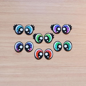 May include: Assortment of colorful googly eyes with black pupils. The eyes are various sizes and have a shiny, iridescent finish.