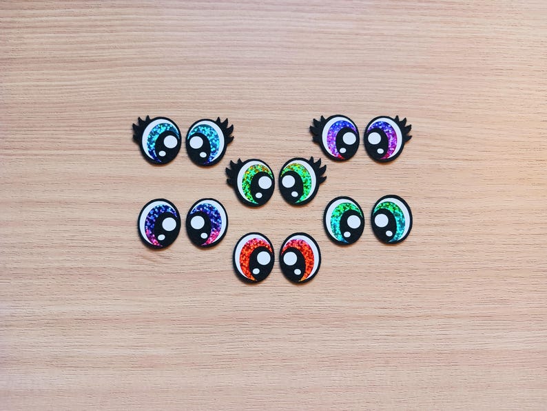 May include: Assortment of colorful googly eyes with black pupils. The eyes are various sizes and have a shiny, iridescent finish.