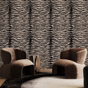 Op de afbeelding: Behang met een herhalend zwart en beige tijgerstrepenpatroon dat de muren bedekt. Twee afgeronde bruine gestoffeerde stoelen staan voor de muur, met een kleine metalen bijzettafel en een zwarte poef in de buurt.