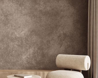 May include: A modern living room scene featuring a beige, rounded armchair with a cylindrical backrest. A small, round stone table with a book sits nearby. The room has a neutral color palette with a textured brown wall and a striped rug.