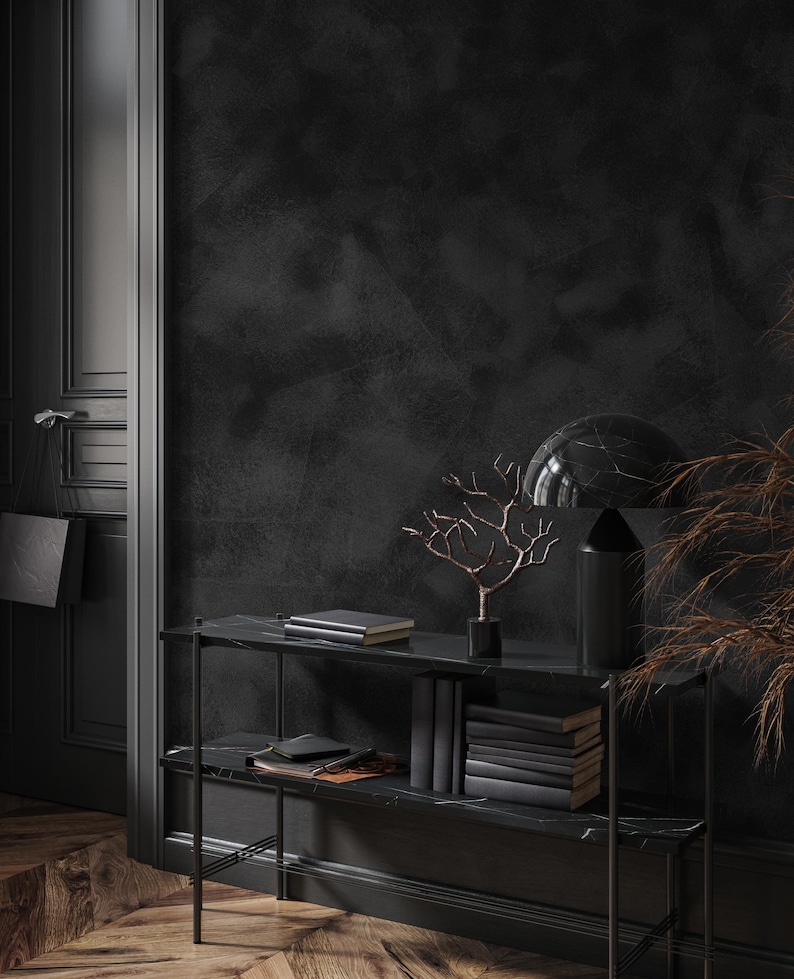 May include: A black marble console table with two shelves, holding books, decorative items, and a small tree sculpture. The background features a dark wall and a door, creating a sophisticated interior design scene.