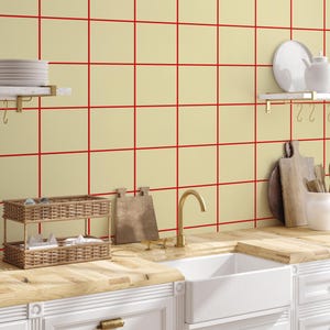 Pode incluir: Interior de cozinha com pia branca, bancadas de madeira e armários brancos. O backsplash amarelo claro tem um padrão de grade vermelha. Cestos de vime, tábuas de corte e uma torneira dourada.