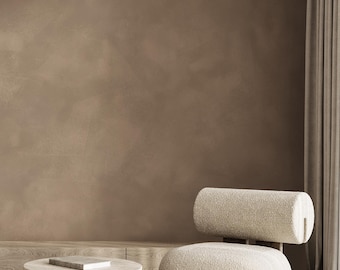May include: A modern living room scene featuring a beige, rounded chair with a cylindrical backrest. A small, round stone table with a book sits nearby. The room has a neutral color palette, with a textured wall and a striped rug.
