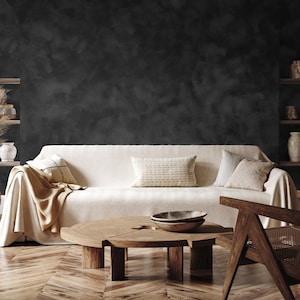 May include: A living room scene featuring a cream-colored sofa with decorative pillows and a tan throw blanket. A round wooden coffee table with a woven top and two wooden bowls sits in front of the sofa. A wooden chair is on the right side of the image.