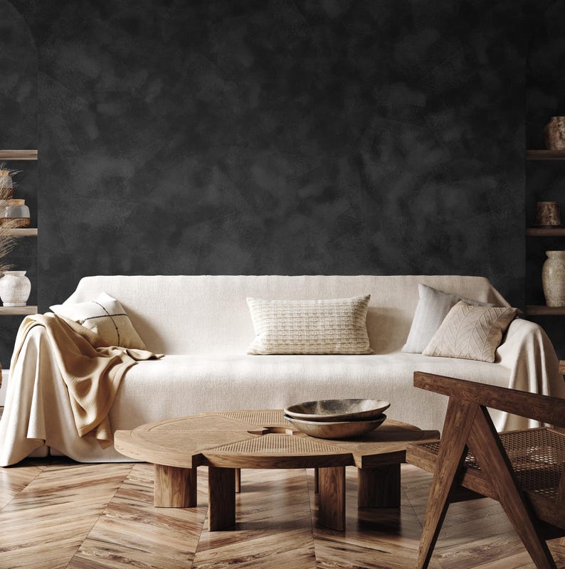 May include: A living room scene featuring a cream-colored sofa with decorative pillows and a tan throw blanket. A round wooden coffee table with a woven top and two wooden bowls sits in front of the sofa. A wooden chair is on the right side of the image.