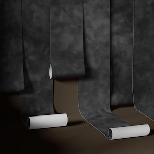 May include: Several rolls of dark gray wallpaper with a textured, mottled appearance are unrolled, revealing white paper cores. The wallpaper hangs against a brown background, creating a contrast.