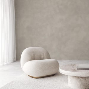 Puede incluir: Un sillón moderno de color crema con un diseño redondeado y una base dorada. La silla está sobre una alfombra blanca texturizada. Una mesa de centro redonda a juego con una tapa de piedra está al lado de la silla. El fondo es una pared neutra y texturizada.