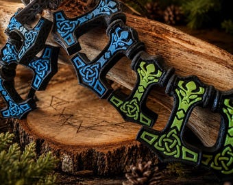 May include: A bracelet composed of multiple black hammer-shaped charms linked together. Each charm features intricate raised knotwork patterns, with some charms highlighted in bright blue and others in vibrant lime green accents.