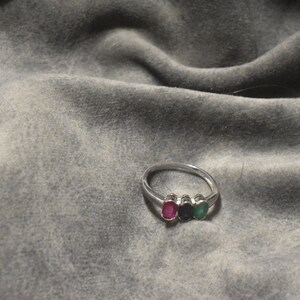 May include: A silver ring with three oval-shaped gemstones. The gemstones are red, blue, and green.