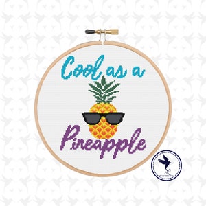 May include: A white embroidery hoop with a cross-stitch design of a pineapple wearing sunglasses and the text "Cool as a Pineapple".