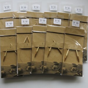 May include: A selection of knitting needles, packaged in clear plastic and brown paper. The needles have light-coloured wooden shafts with gold-coloured tips. Each package has a label with the text "8 Seeknit" and size information.
